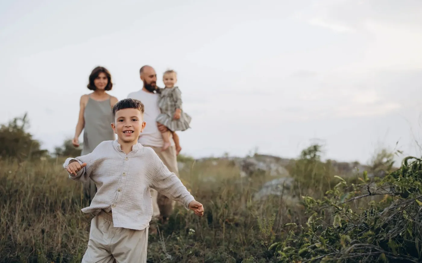 A family joyfully running together through a lush green field under a clear blue sky.